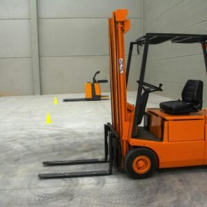 An orange forklift in a spacious warehouse with concrete floors and minimal equipment.